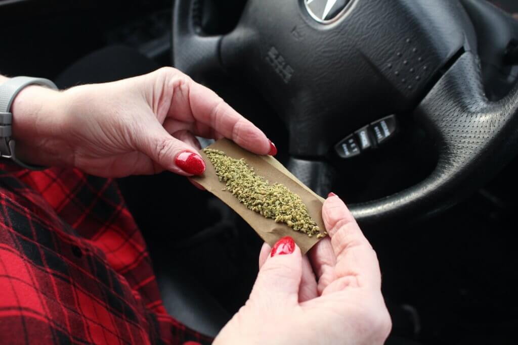Woman rolling joint while driving car