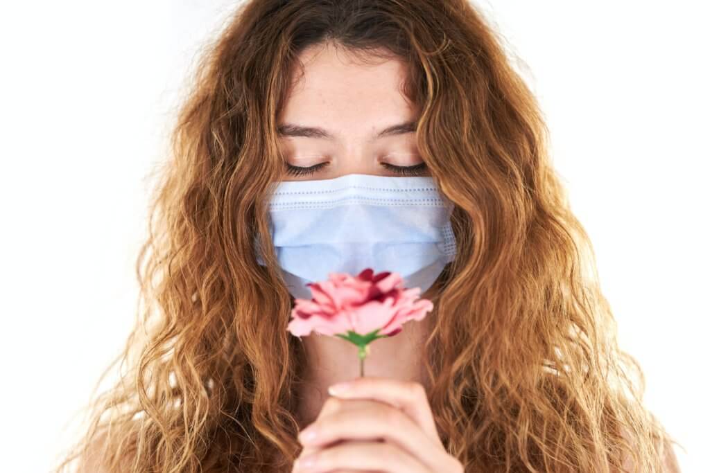 Woman smelling a flower with a face mask on
